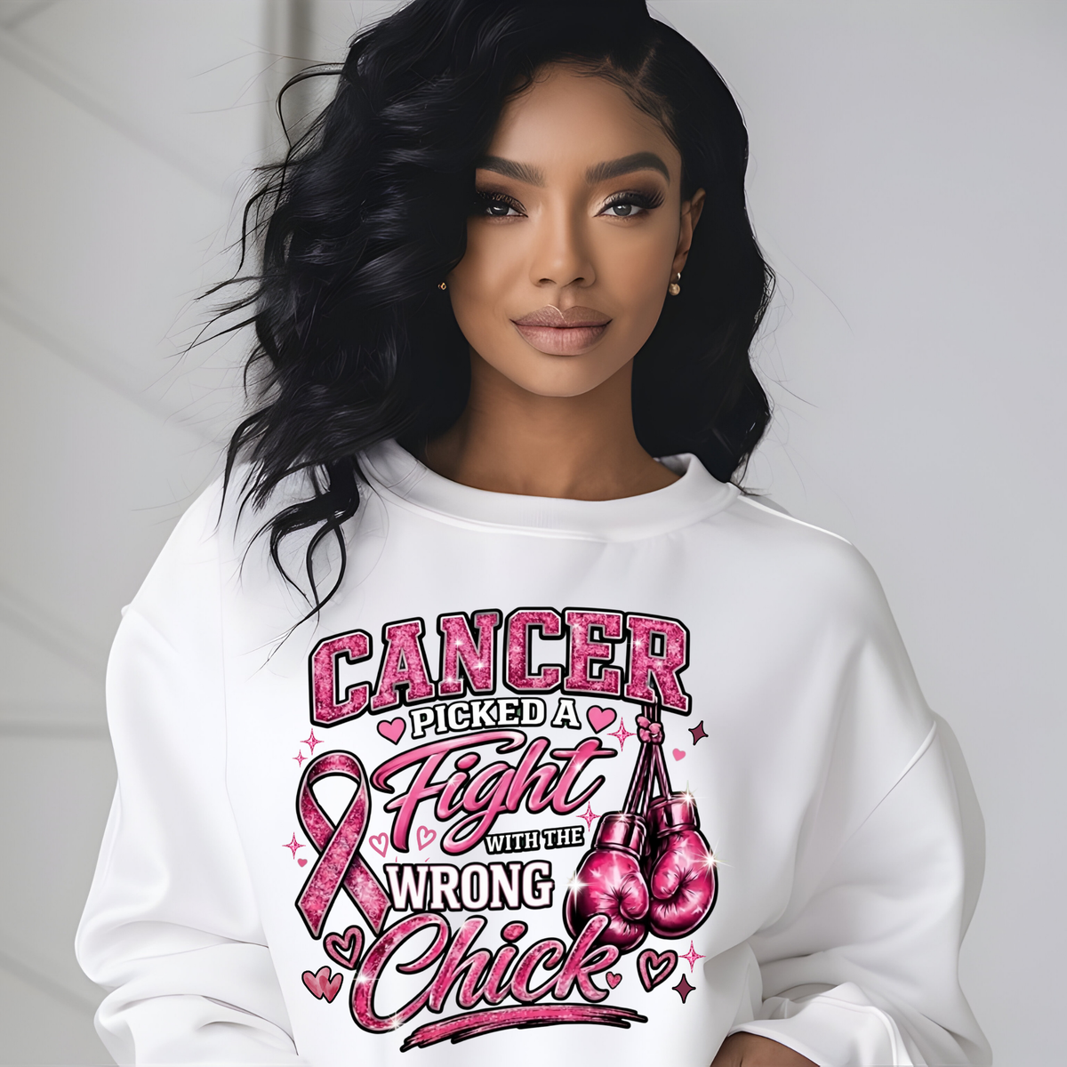 A woman wearing a white crewneck sweatshirt with a graphic print that reads 'HER Fight IS OUR Fight' in pink and black lettering, featuring three Black women and a pink ribbon. The background is a clean, light gray wall.