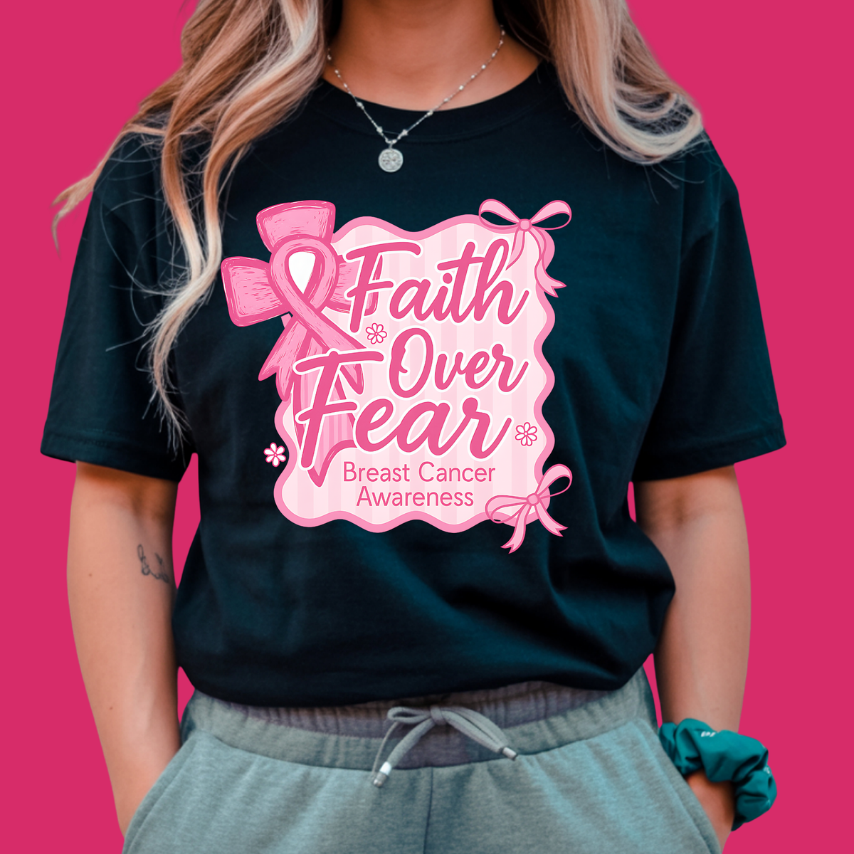 Person wearing a black t-shirt with 'Faith Over Fear' breast cancer awareness design on a pink background  Pink Ribbon Tee: Faith Over Fear - Supportive Awareness T-shirt