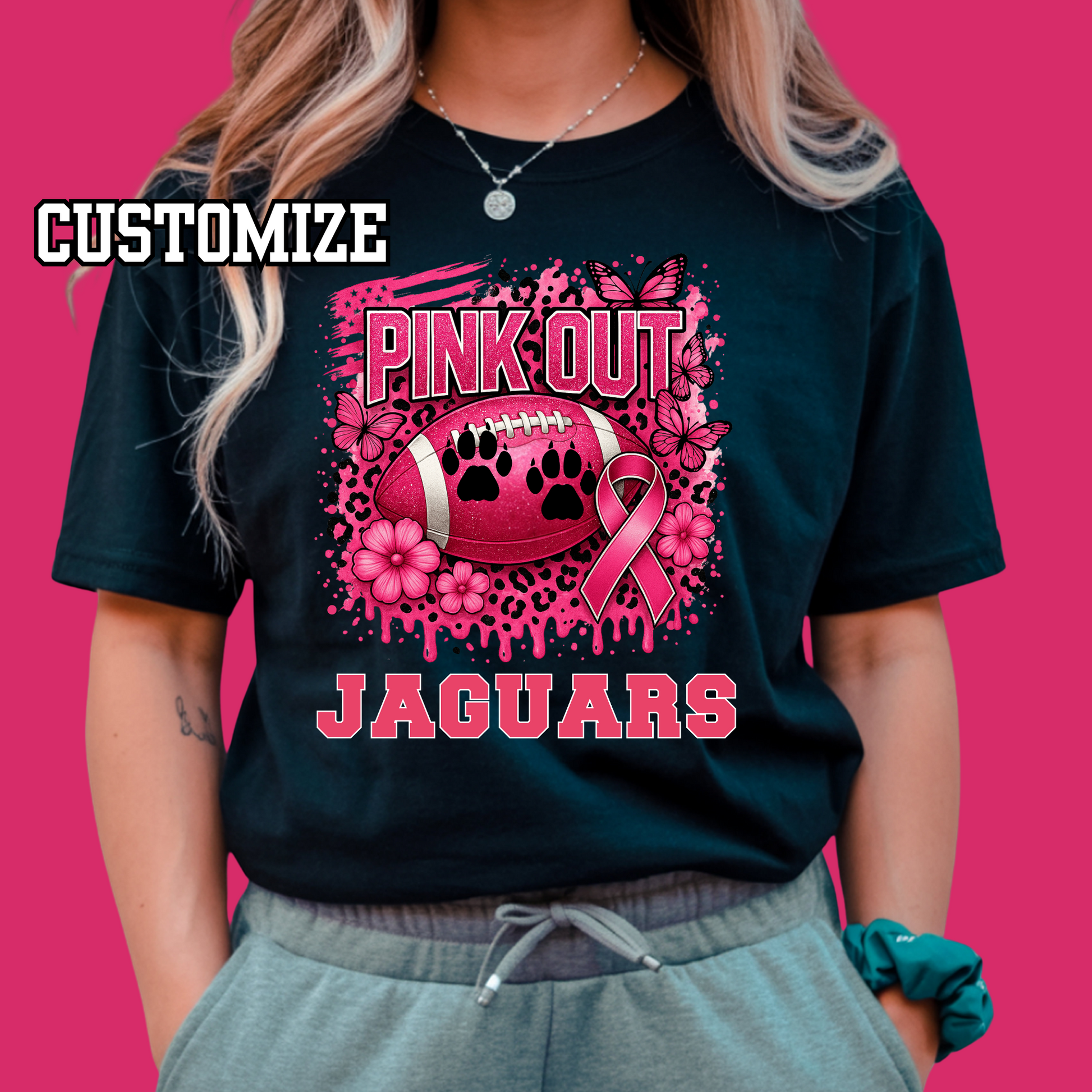 Person wearing a black t-shirt with pink 'Pink Out Jaguars' design on a pink background Custom Pink Out Football Tee - Custom Pink Out Mascot T-Shirt