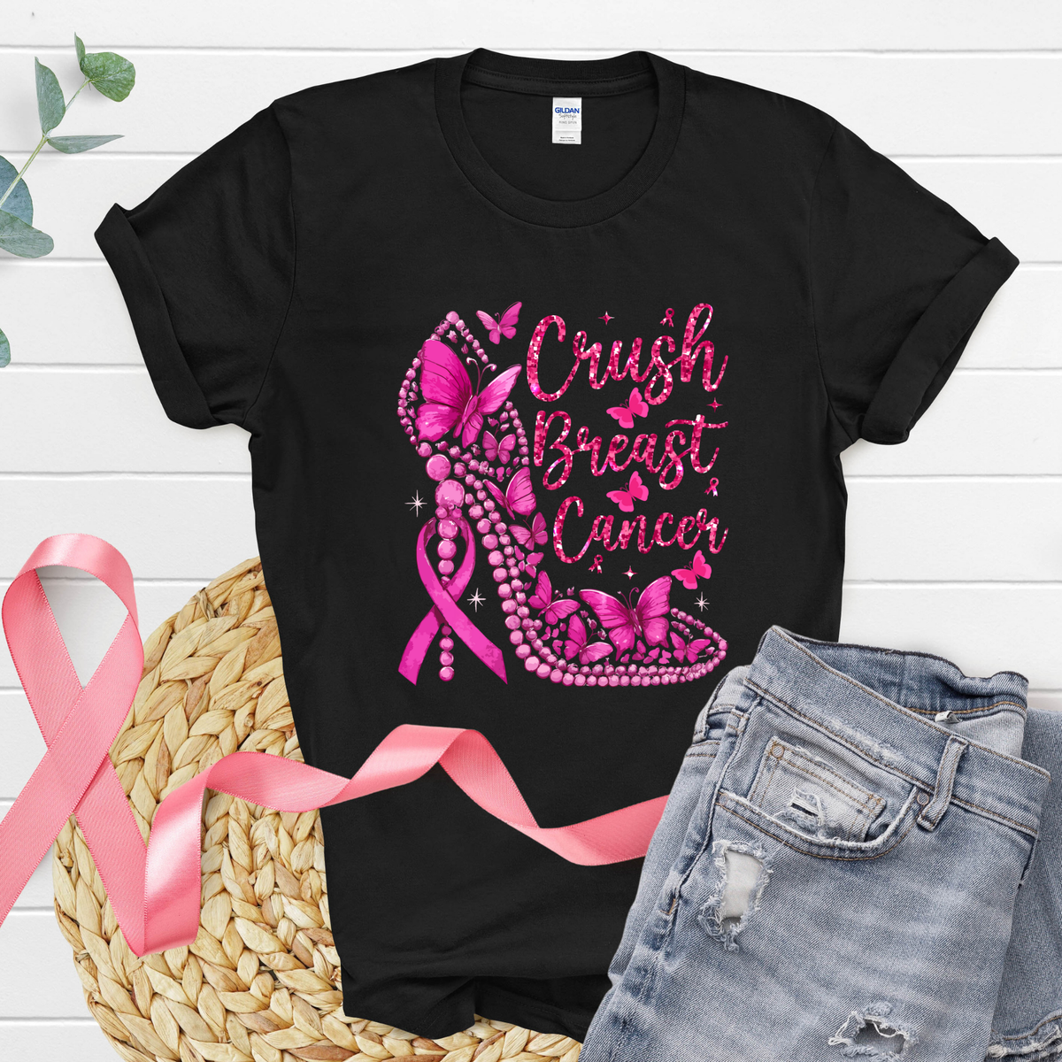 Black t-shirt with pink breast cancer awareness design, pink ribbon, and jeans on a wooden surface.