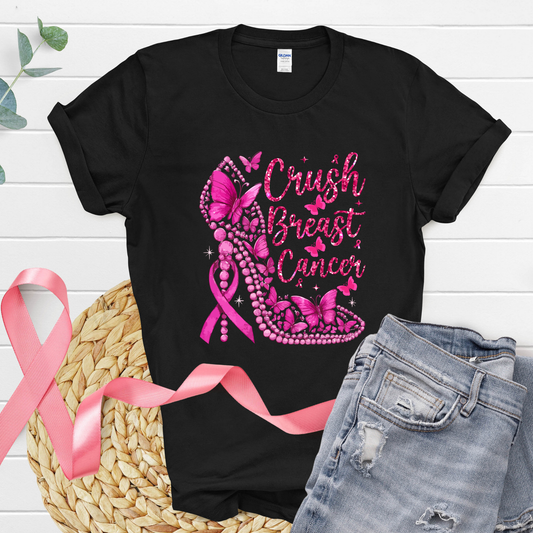 Black t-shirt with pink breast cancer awareness design, pink ribbon, and jeans on a wooden surface.