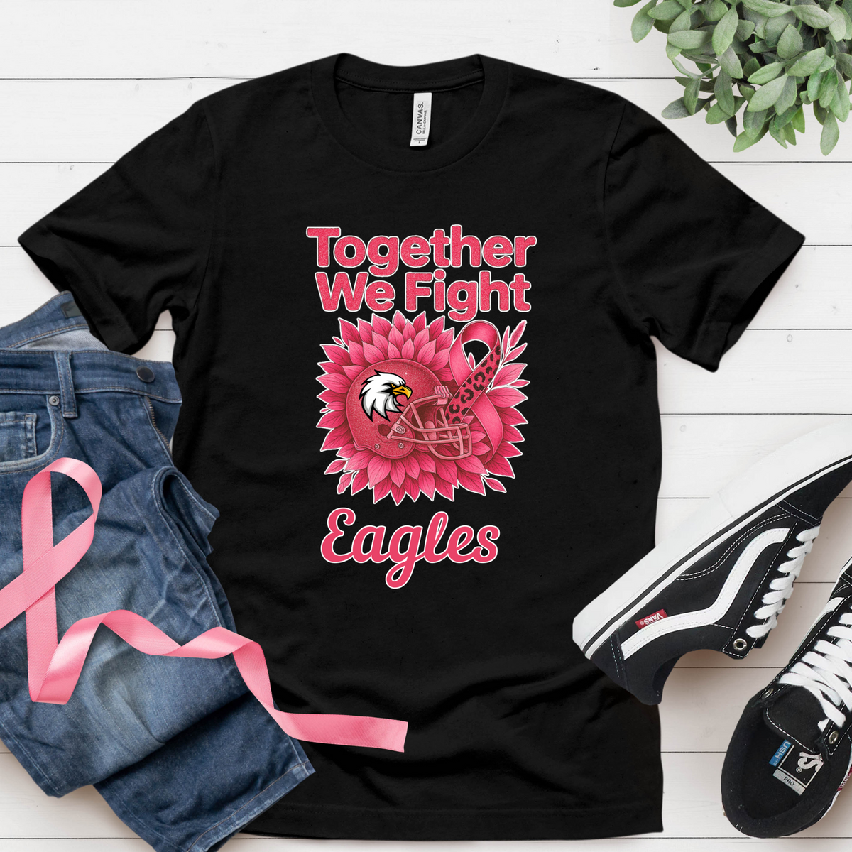 Black t-shirt with pink eagle design and text on a white wooden surface with jeans and sneakers.