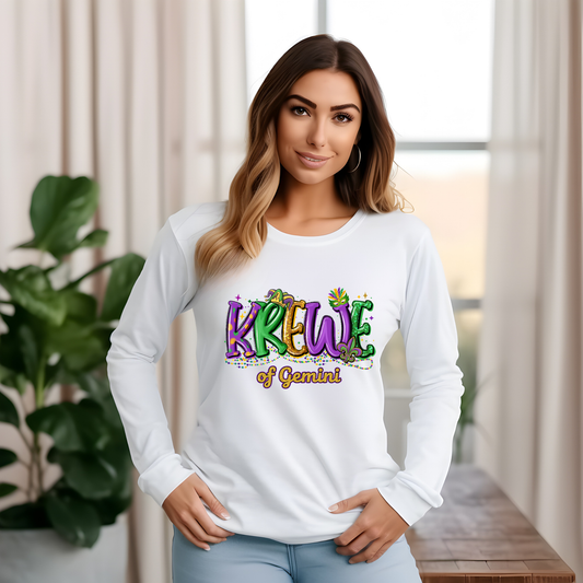 Woman wearing a white long-sleeve shirt with 'KREWE of Gemini' design in a bright room.