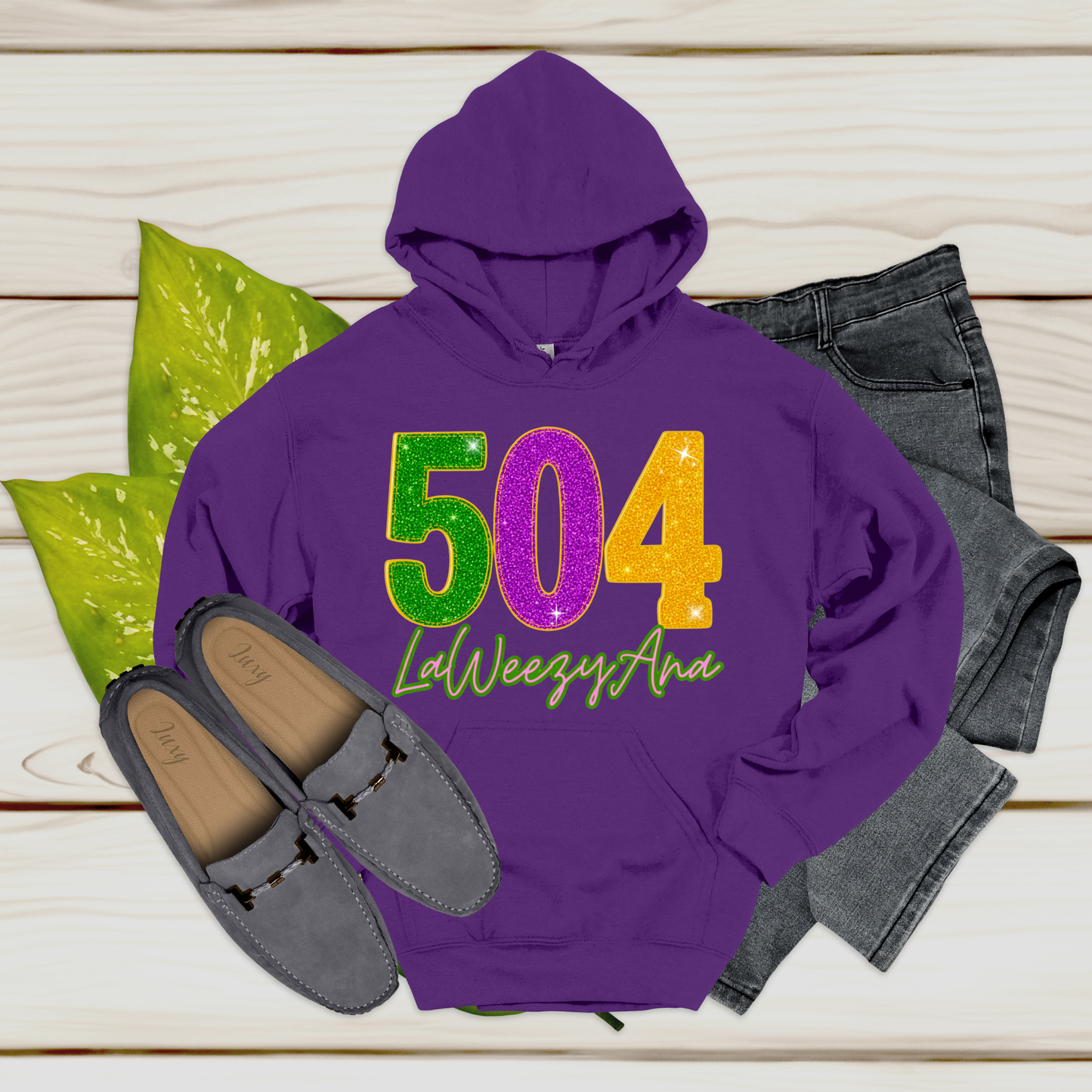 Purple hoodie with decorative numbers and text, paired with jeans and loafers on a wooden surface.