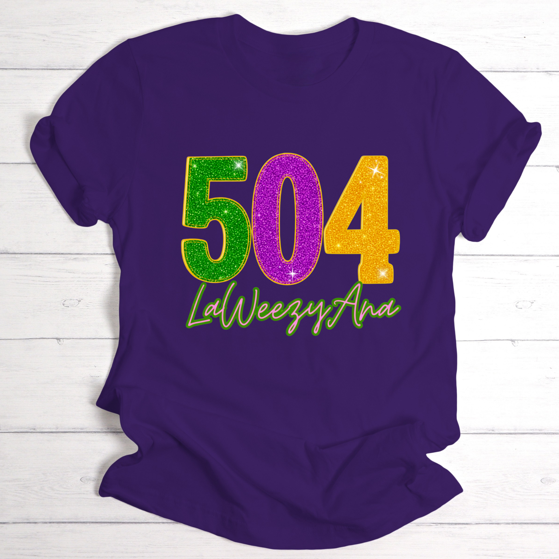 Purple t-shirt with colorful '504 LaWeezyAna' design on a wooden surface
