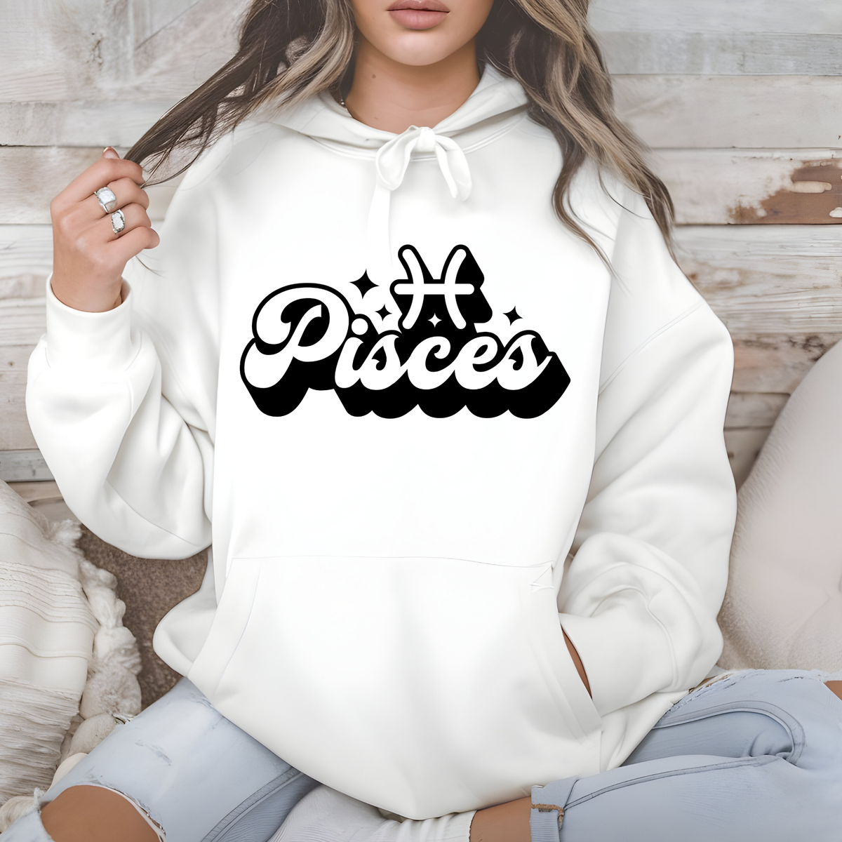 A woman wearing a white pullover hoodie with a black 'My Scorpio' graphic printed on the chest, sitting against a rustic wood panel background.