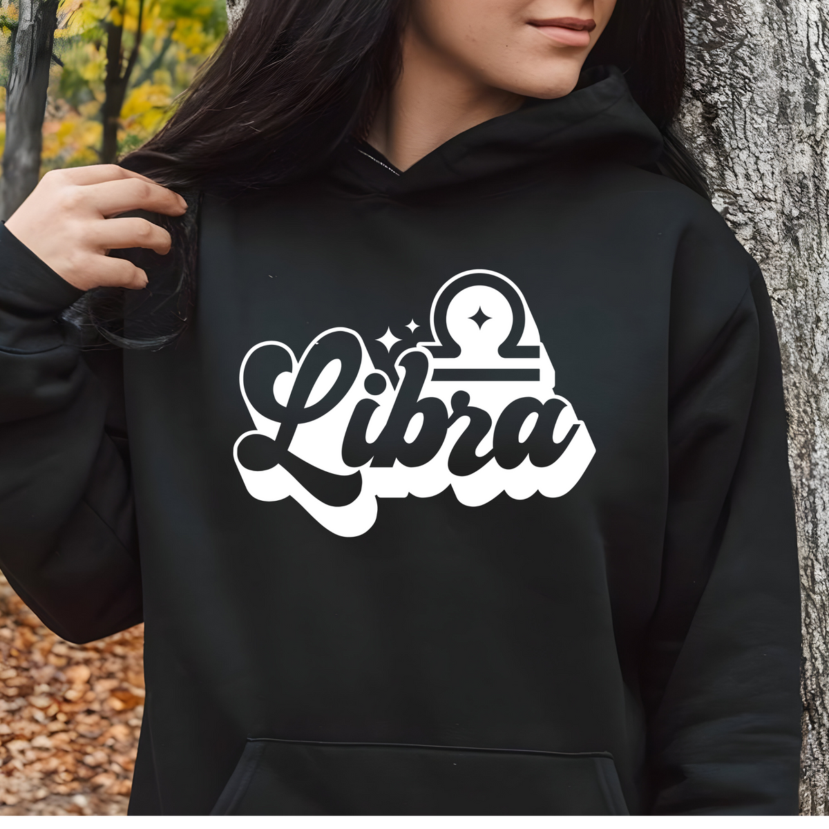 A person wearing a black pullover hoodie with a large white and black 'My Virgo' graphic on the chest, standing outdoors next to a tree trunk.