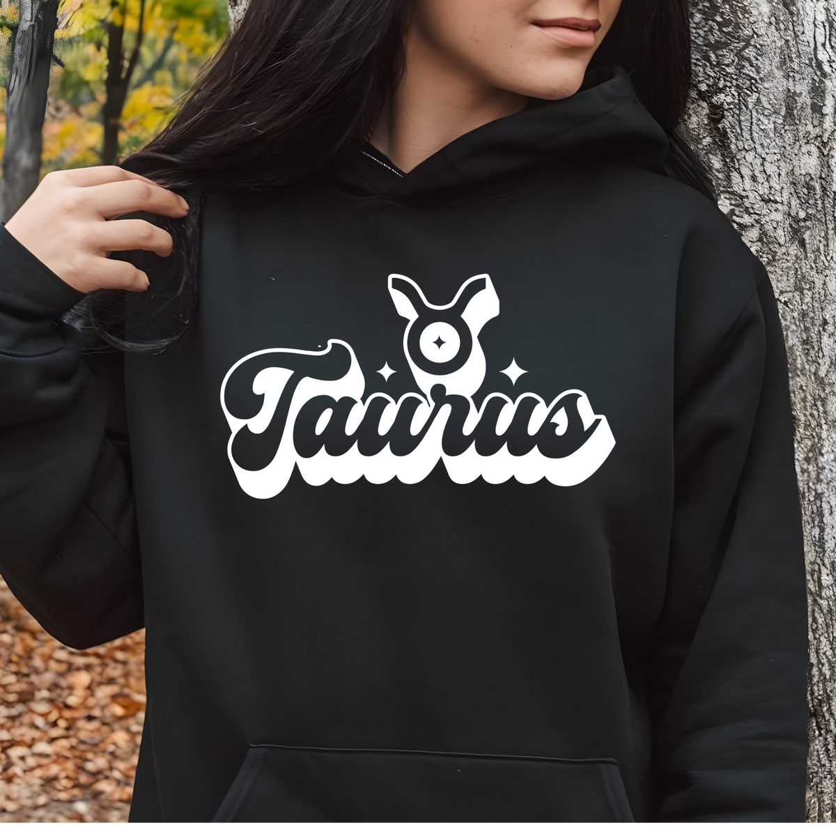 A person wearing a black pullover hoodie with a large white and black 'My Virgo' graphic on the chest, standing outdoors next to a tree trunk.