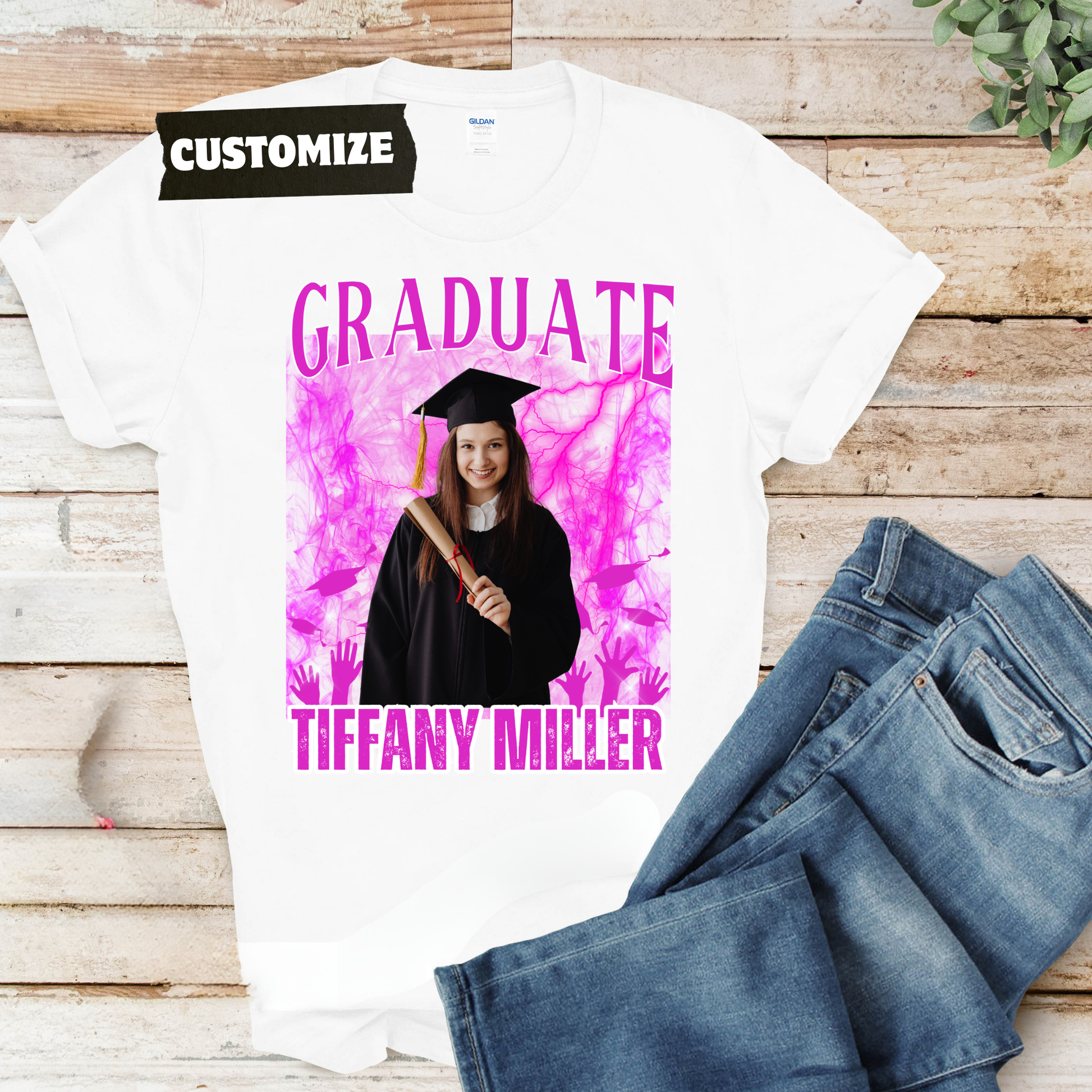 Graduation-themed t-shirt with a photo of a graduate and text on a wooden surface with jeans.  Customizable graduation photo t-shirt featuring senior portrait, school mascot, and sports organization logos in school colors