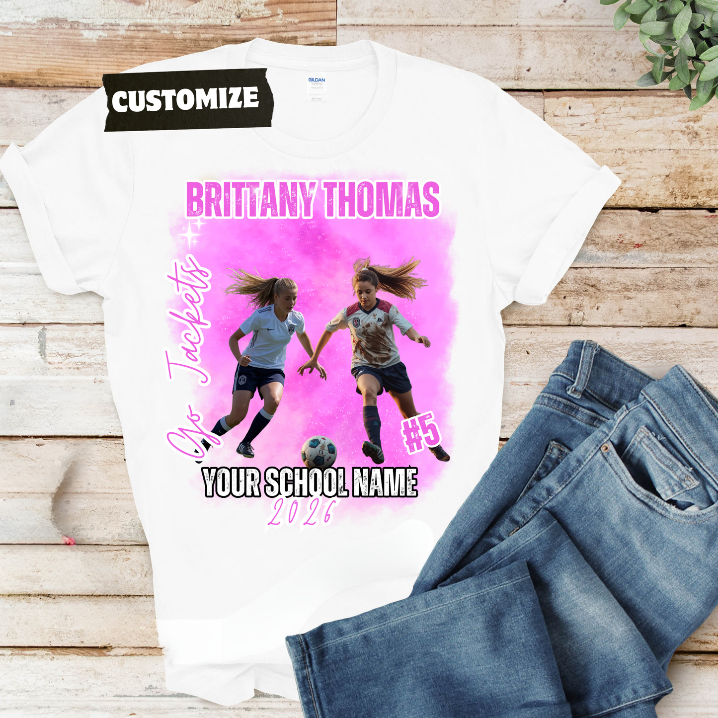 White t-shirt with soccer-themed design and jeans on a wooden surface