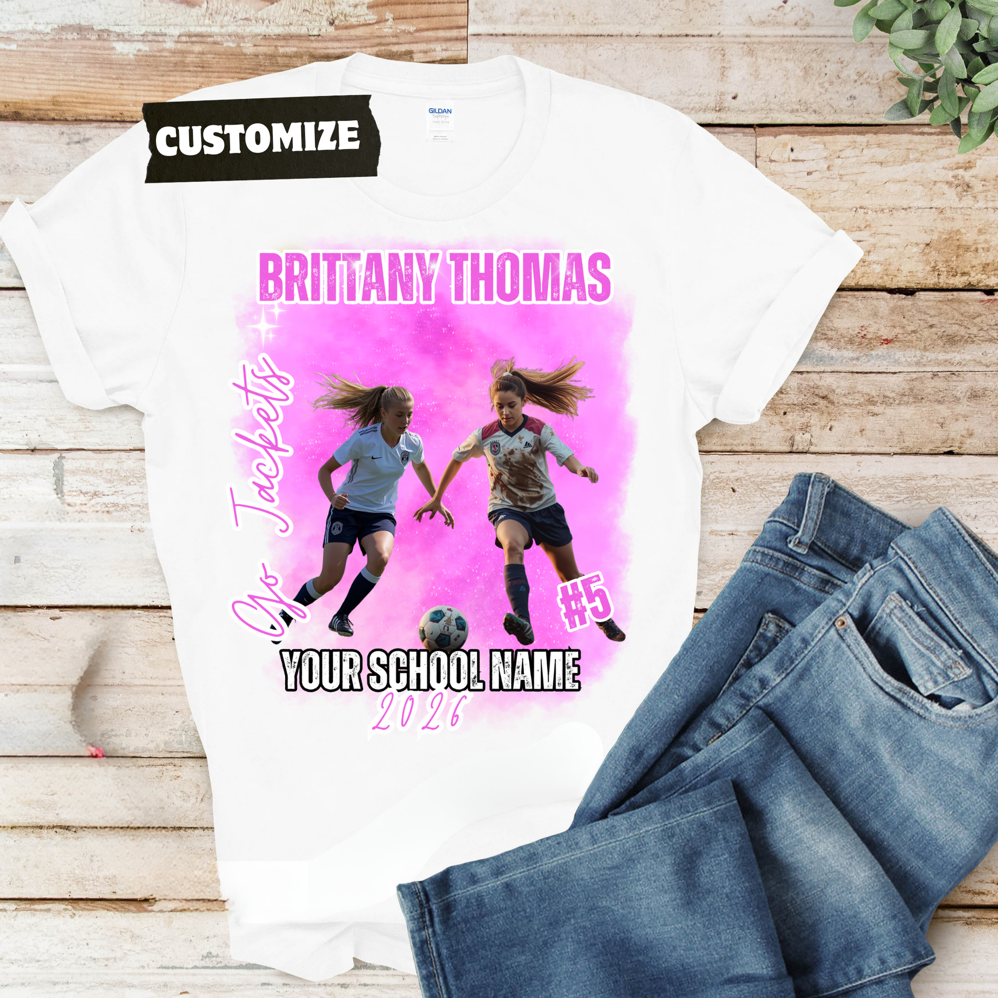 White t-shirt with soccer-themed design and jeans on a wooden surface