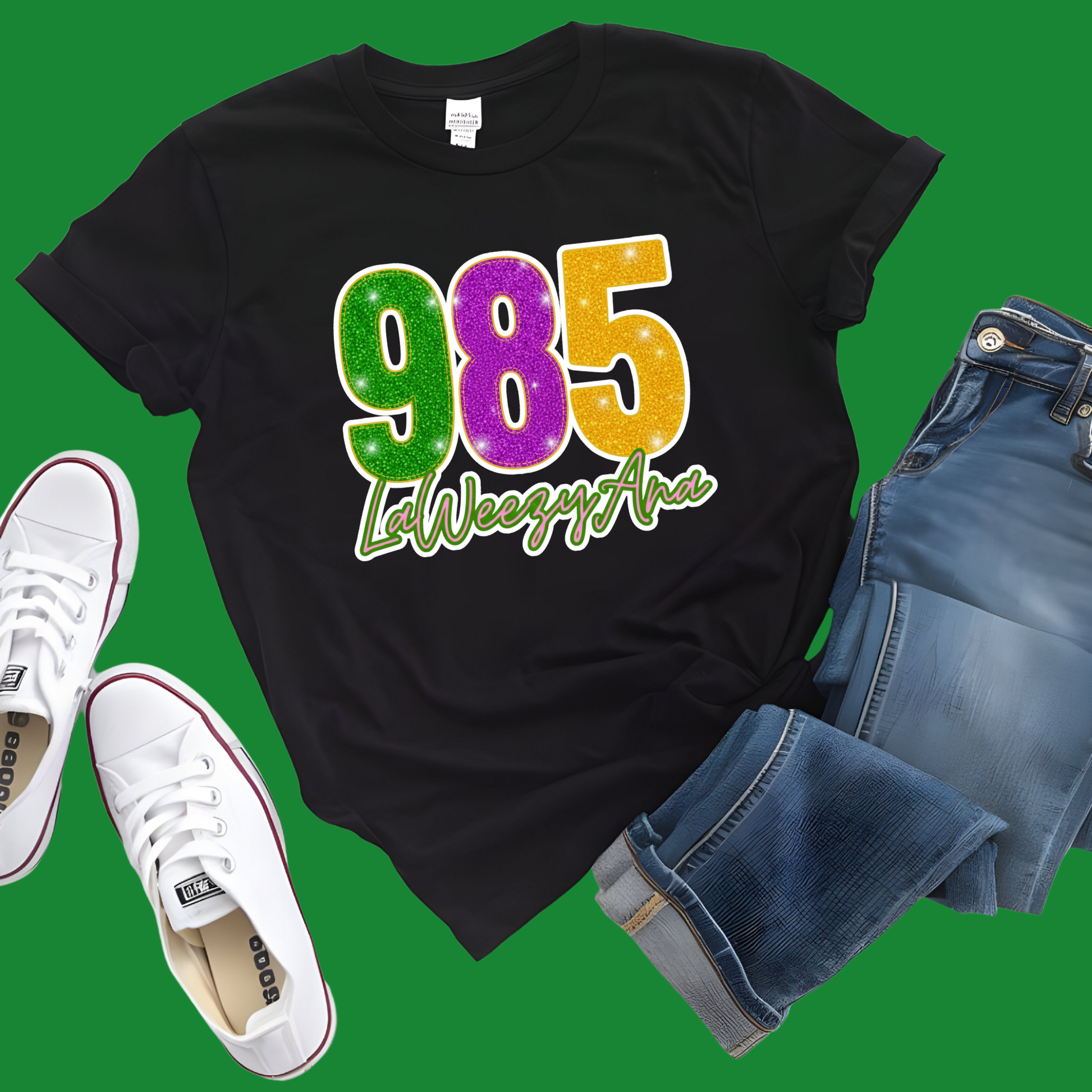 Black t-shirt with colorful '985 LeWeezyAna' design, white sneakers, and blue shorts on a green background
