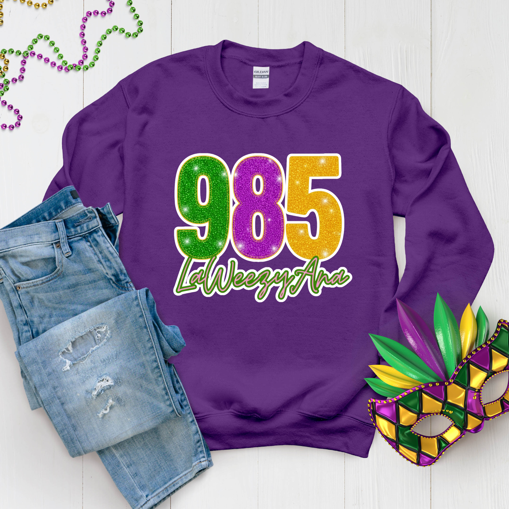 Purple sweatshirt with '985 La Weezy Ana' text, denim shorts, and Mardi Gras mask on a white background