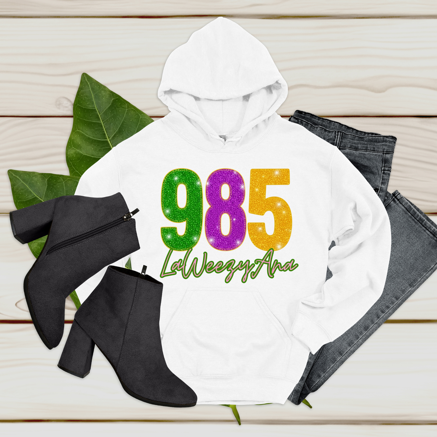 White hoodie with colorful text, black boots, and jeans on a wooden surface