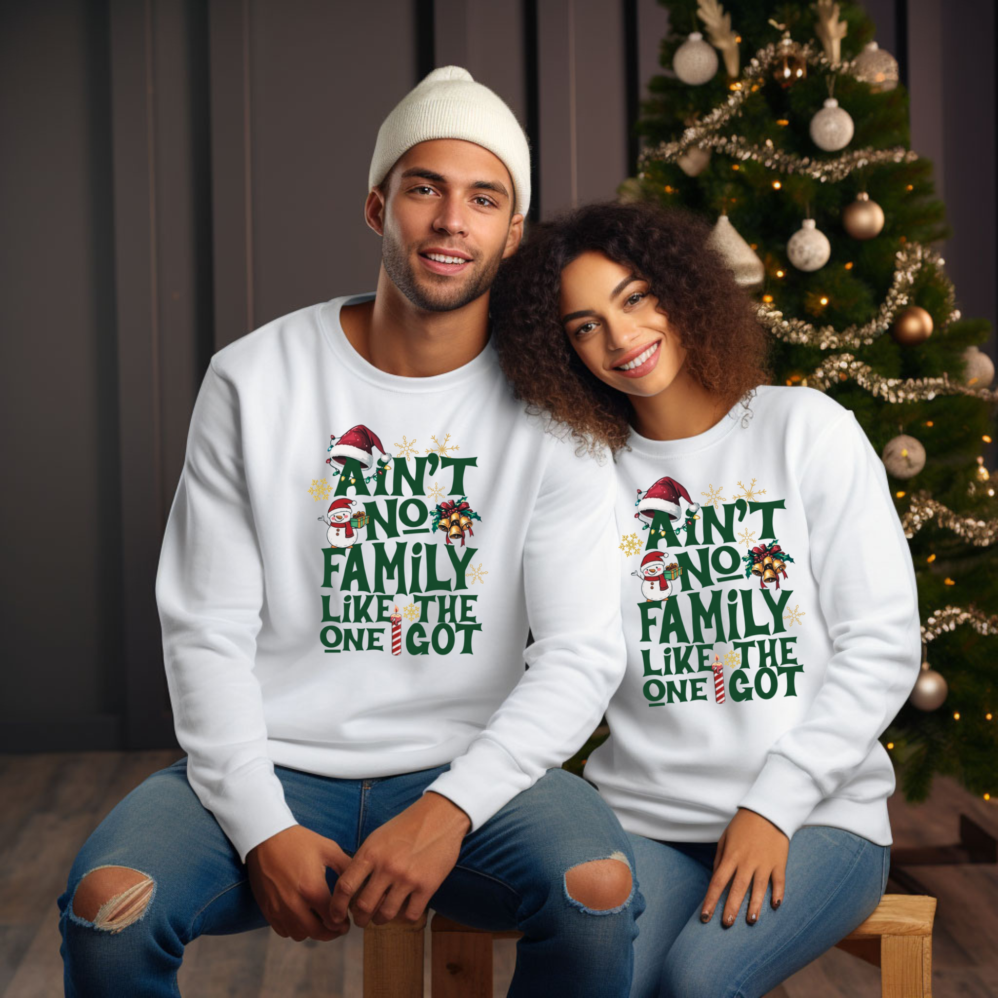 Two people wearing matching white sweatshirts with Christmas-themed text in front of a decorated Christmas tree.