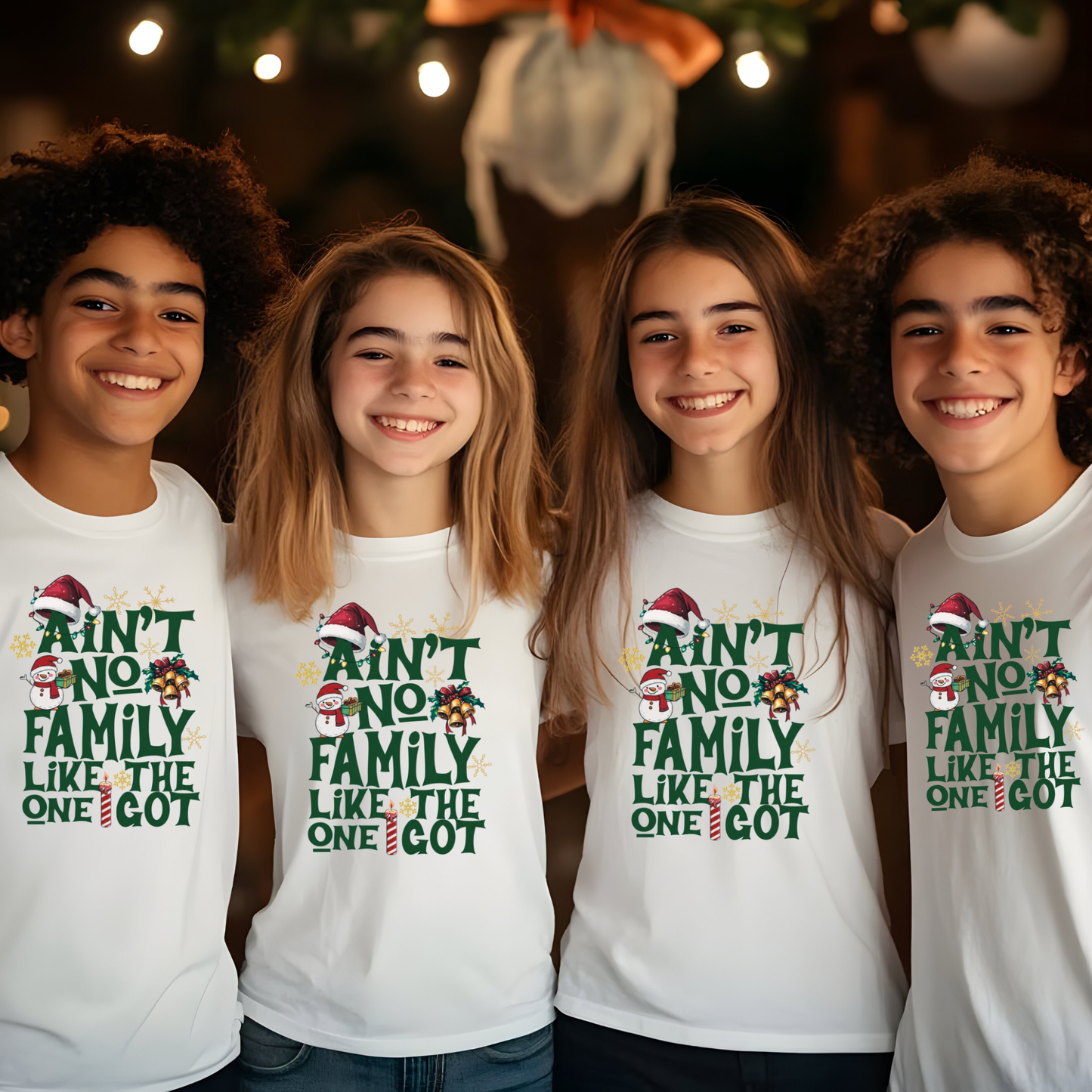 Four children wearing white t-shirts with Christmas-themed text, standing in front of a decorated Christmas tree.