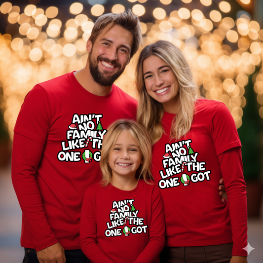 Family of three wearing matching red sweatshirts with a humorous family-themed design against a blurred festive background.