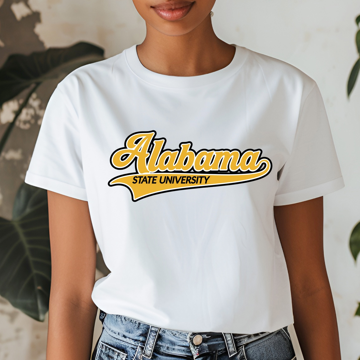 A woman wearing a white short-sleeve graphic T-shirt with 'Alabama State University' printed in yellow and black across the chest, paired with blue jeans.