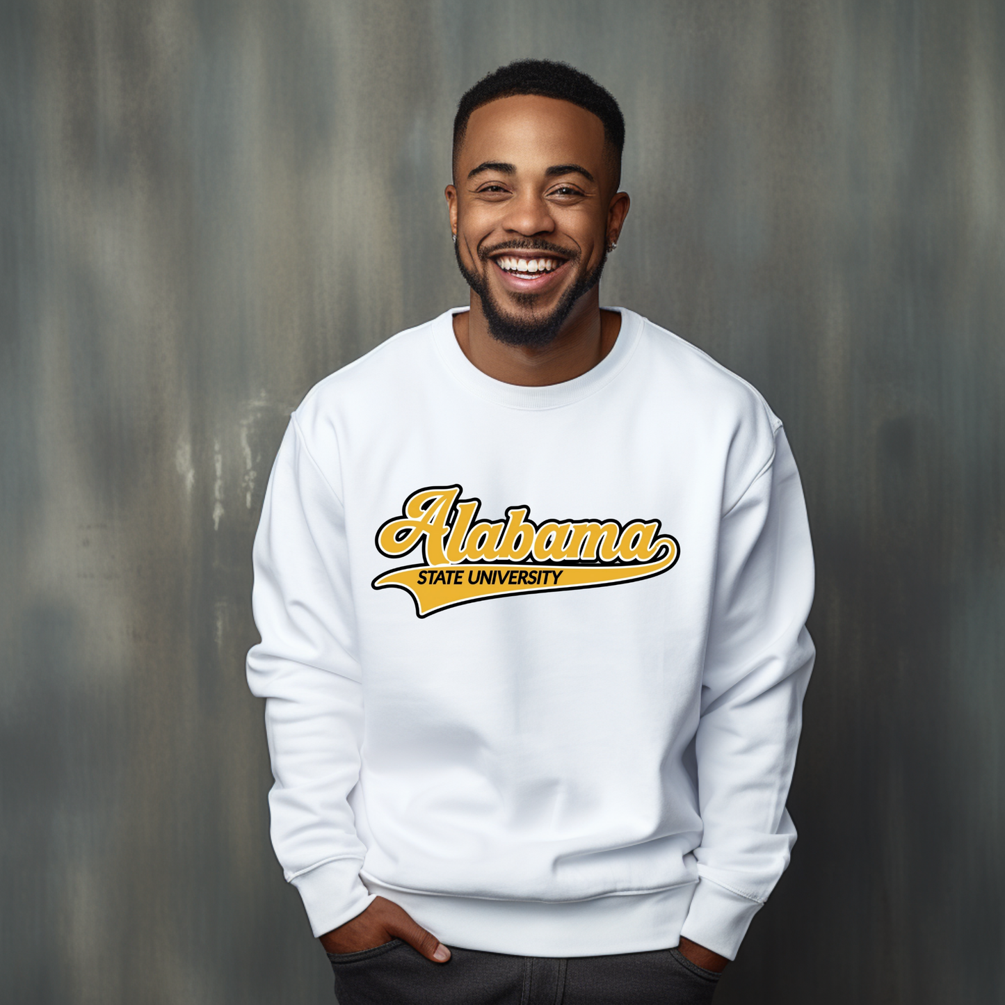 A smiling man wearing a white crewneck sweatshirt with a yellow and gold 'Alabama State University' graphic on the front, set against a textured gray studio background.