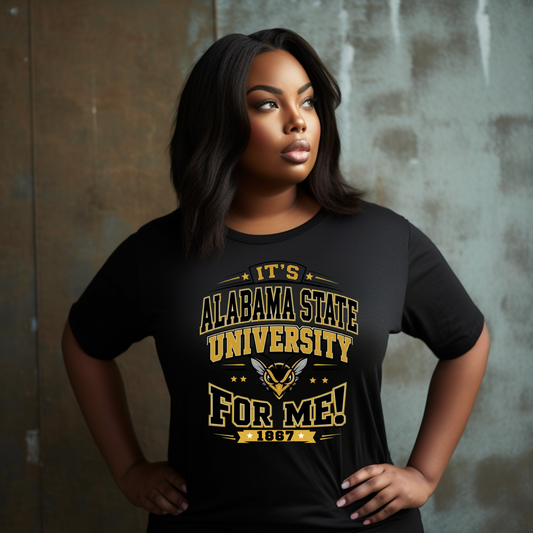 A woman wearing a black short-sleeve graphic T-shirt with gold text reading 'IT'S ALABAMA STATE UNIVERSITY FOR ME! 1867' and a winged emblem, posed against a textured gray-brown wall.