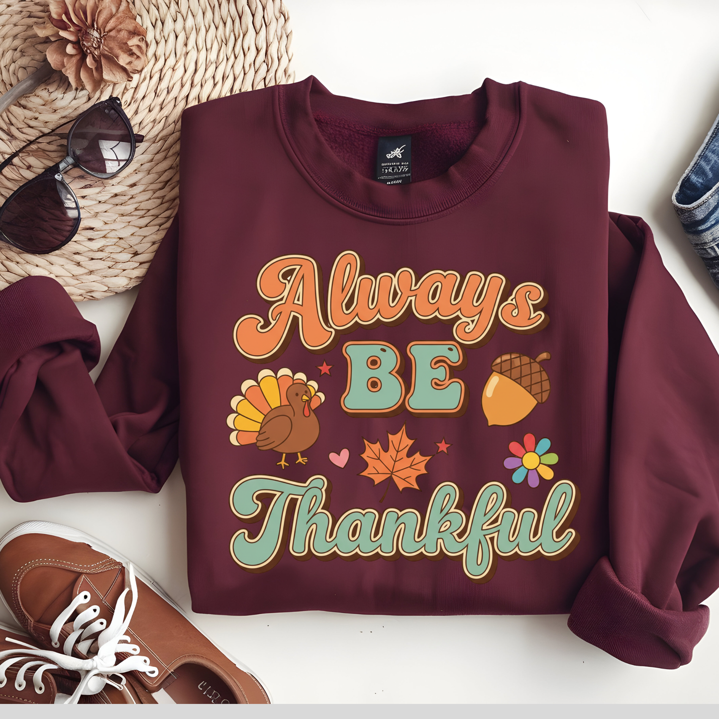 Maroon sweatshirt with 'Always Be Thankful' text and graphics on a white surface with accessories.  Retro Thanksgiving Sweatshirt "Always Be Thankful" Fall Harvest Crewneck Sweater