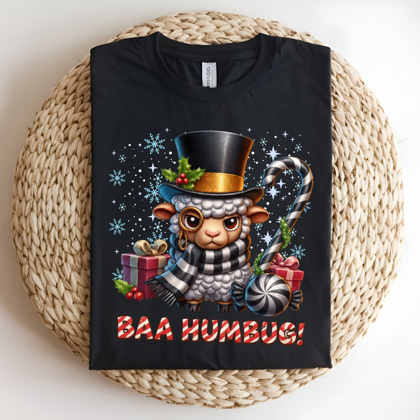 Black t-shirt with a Christmas-themed design of a sheep wearing a top hat and scarf, surrounded by presents and candy canes, on a woven mat.