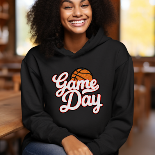 Person wearing a black hoodie with 'Game Day' and basketball design, sitting indoors.