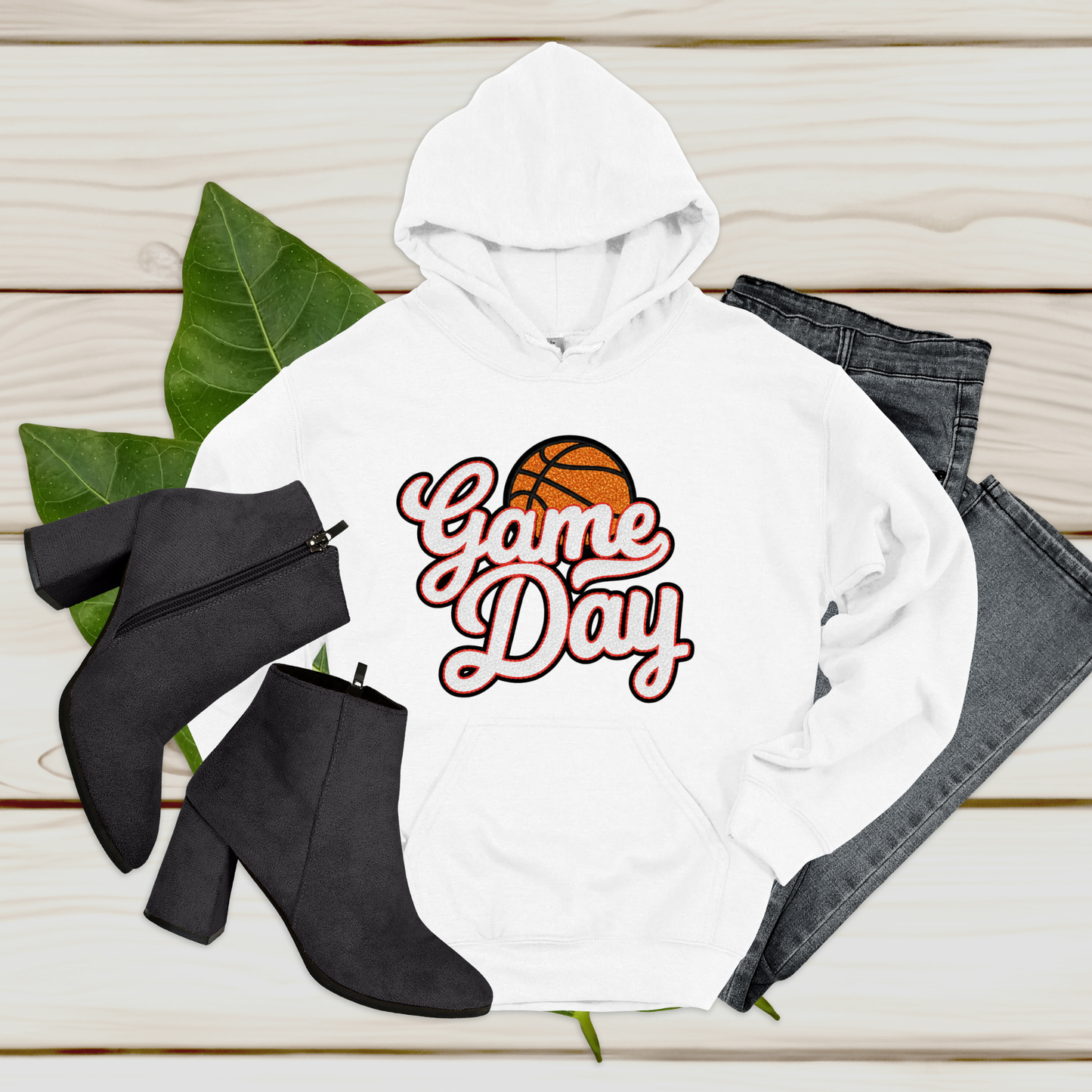 White hoodie with 'Game Day' and basketball graphic, black boots, and jeans on a wooden surface.