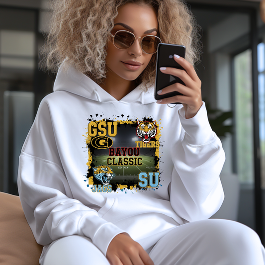 Woman wearing a white hoodie with a sports team logo, sitting and looking at her phone. Bayou Classic Football Hoodie - Grambling State GSU Tigers vs. Southern University SU Jags Hoodie