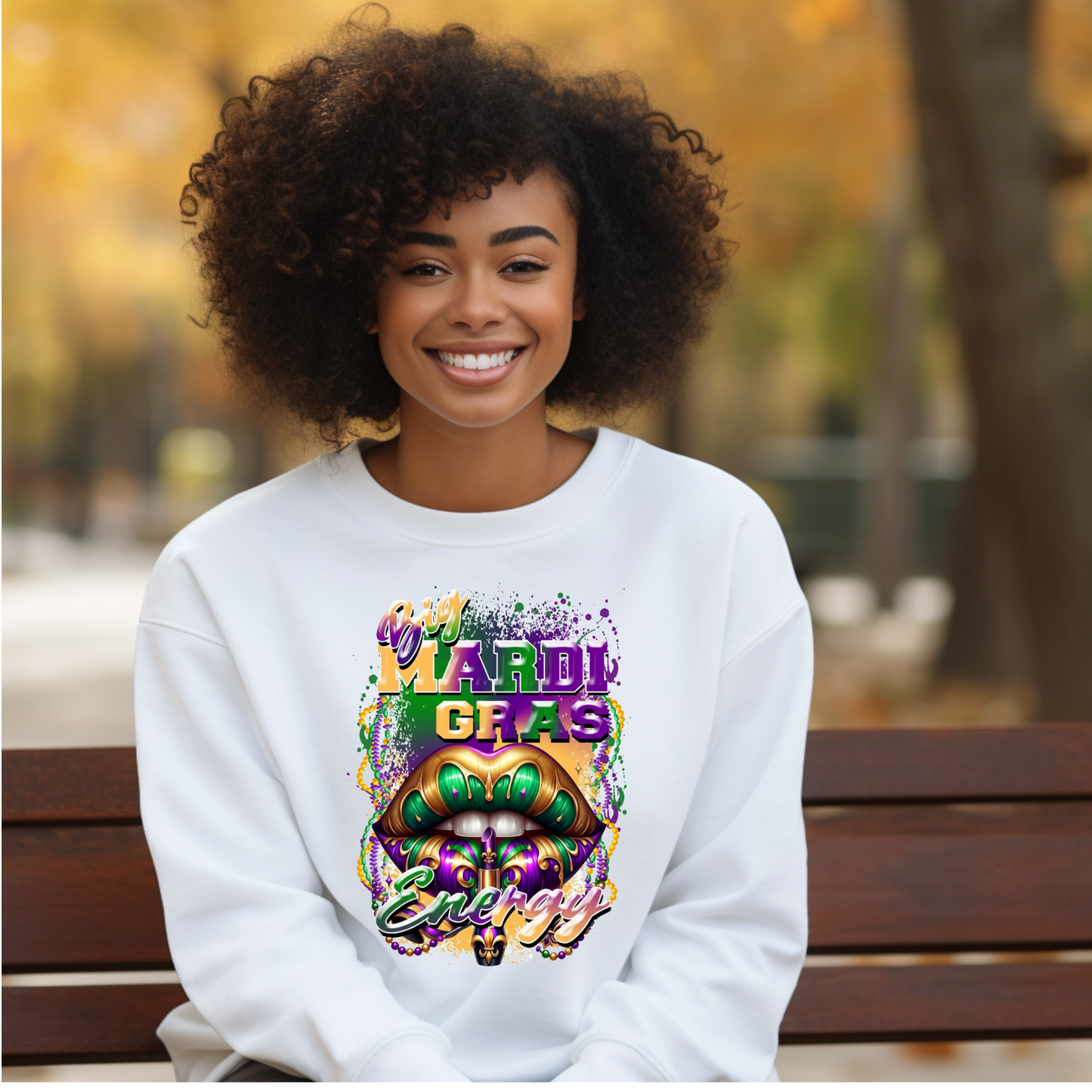 Woman wearing a white sweatshirt with Mardi Gras-themed design sitting on a bench outdoors.