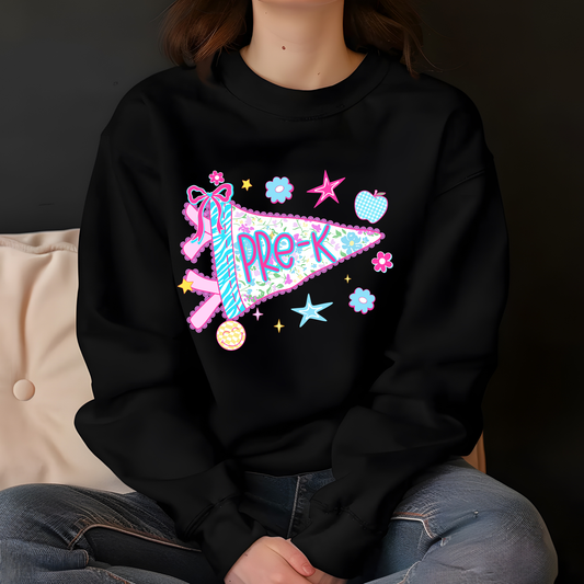 A person wearing a black crewneck sweatshirt with a colorful 'Pre-K' pennant graphic on the chest, paired with blue jeans, sitting against a dark background.