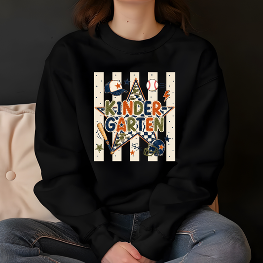A person wearing a black crewneck sweatshirt with a colorful 'KINDERGARTEN' baseball graphic on the front, paired with blue jeans, sitting against a dark background.