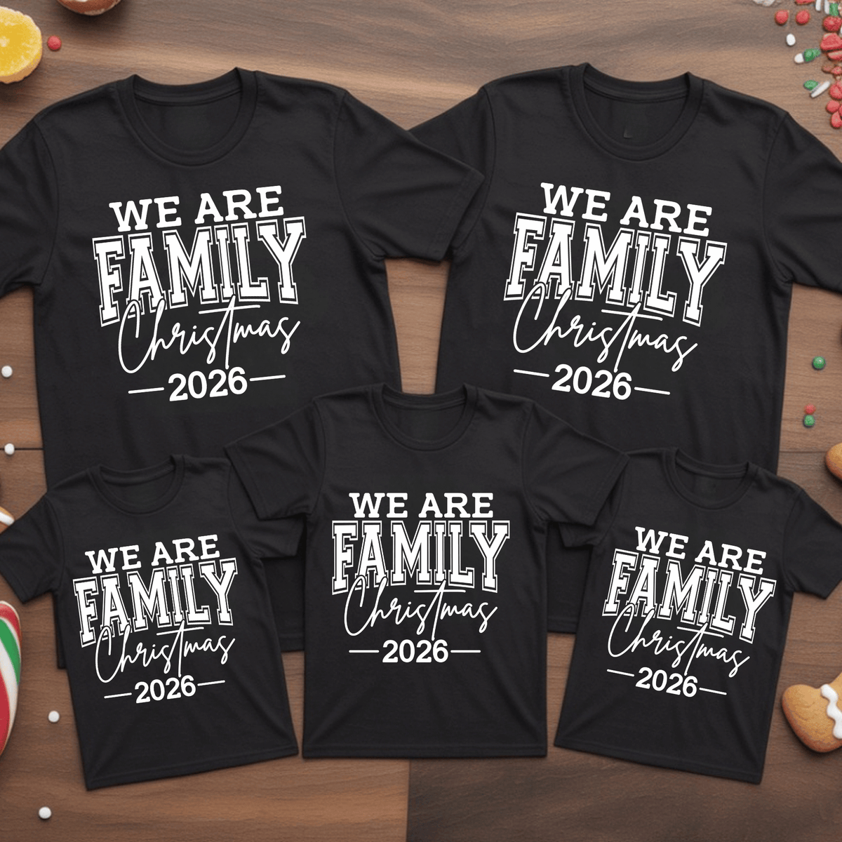 Set of five black matching family t-shirts printed with white 'We Are Family Christmas 2026' collegiate typography on a wooden backdrop.