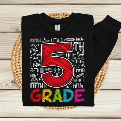 A black long-sleeve t-shirt with a colorful 'Fifth Grade' graphic, displayed flat on a woven placemat over a light wood background.