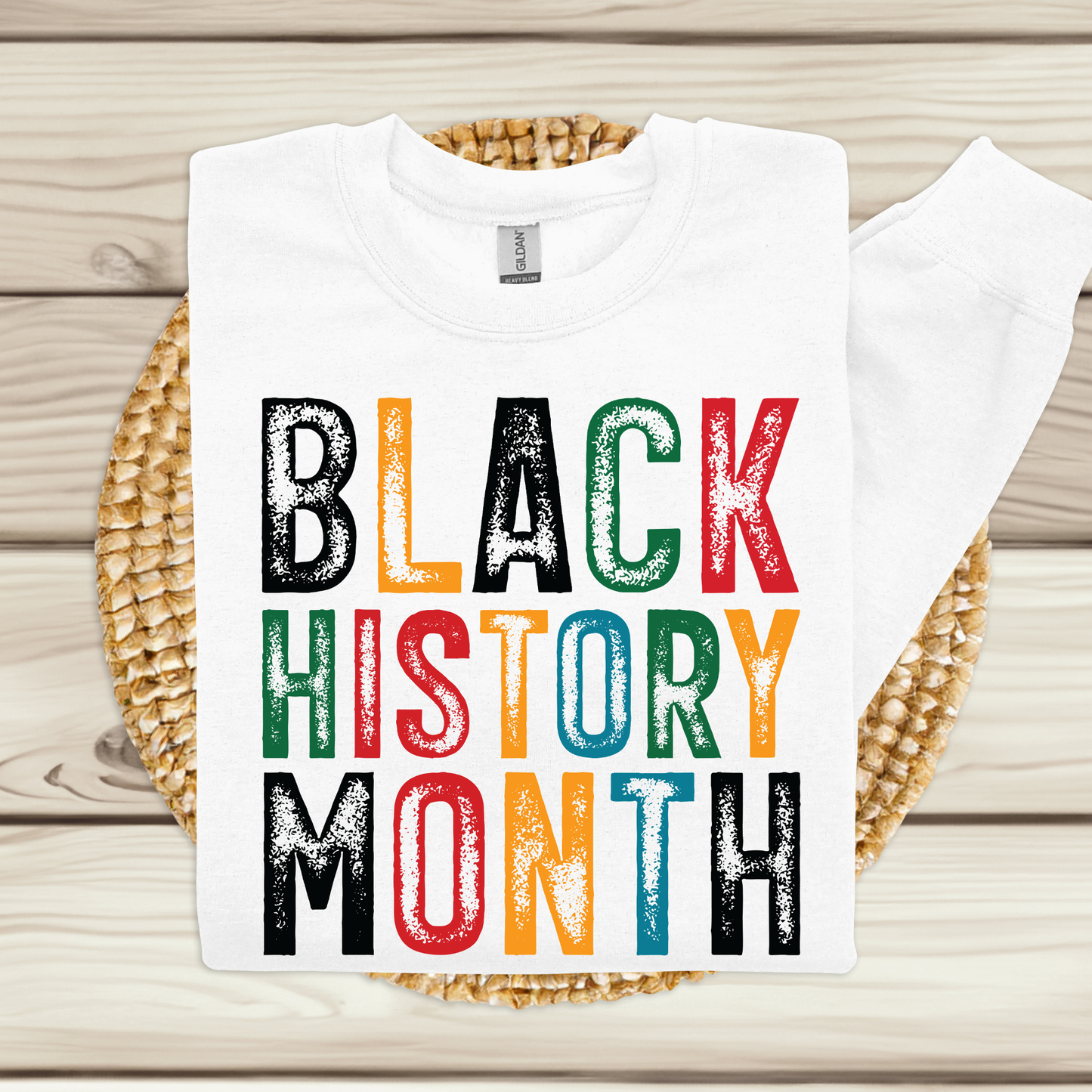 White t-shirt with 'BLACK HISTORY MONTH' in multicolor on a woven mat.