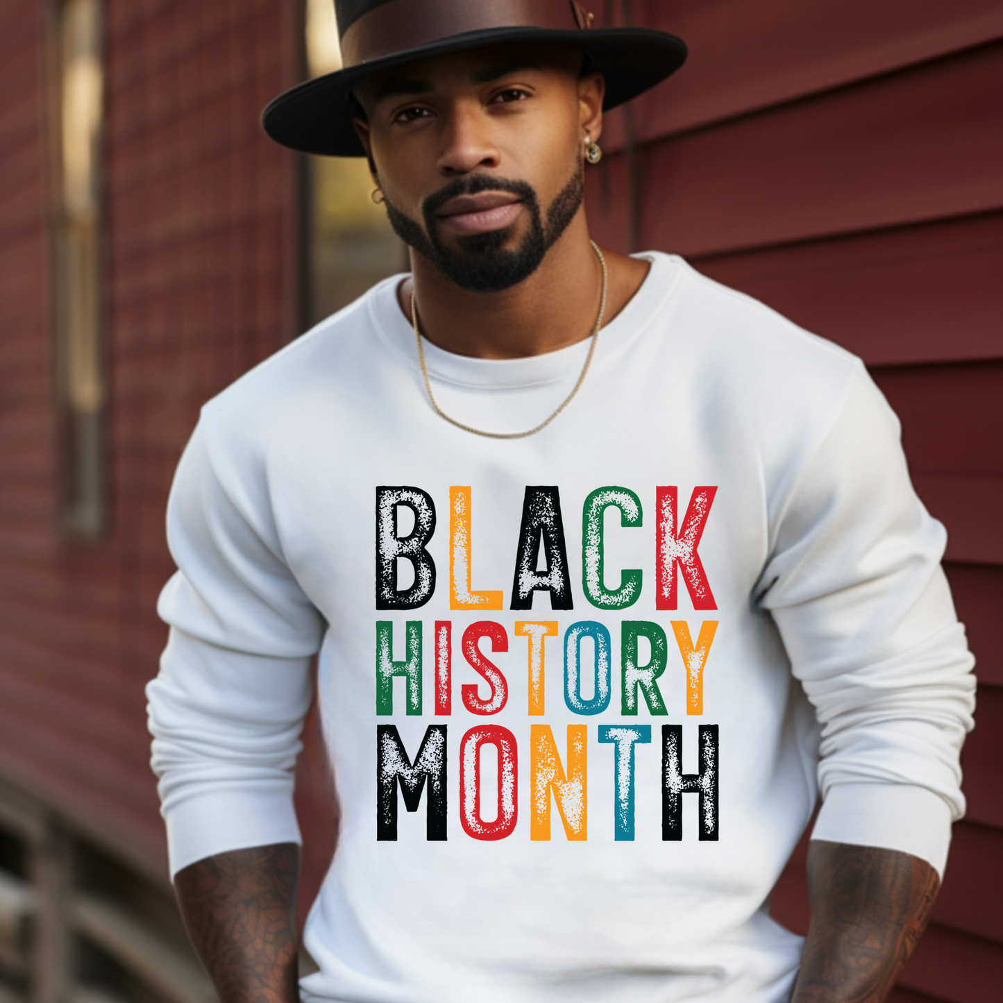 Man wearing a white sweatshirt with 'BLACK HISTORY MONTH' in colorful letters against a red wooden background.