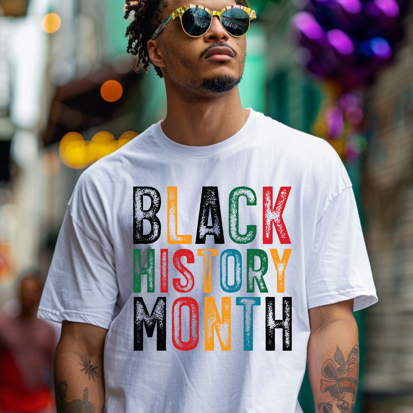 Person wearing a white t-shirt with 'BLACK HISTORY MONTH' in colorful letters on a blurred street background.