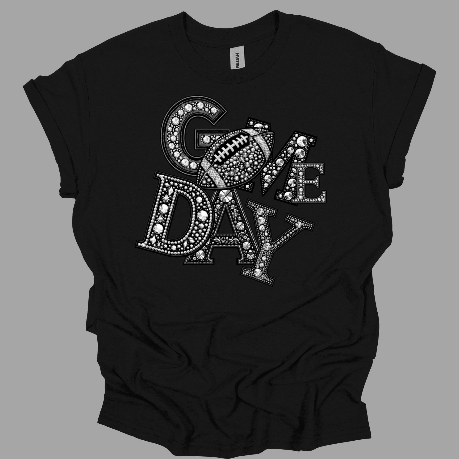 A black short-sleeve t-shirt with a 'GAME DAY' graphic made of letters filled with white rhinestones and a football motif, shown on a solid gray background.