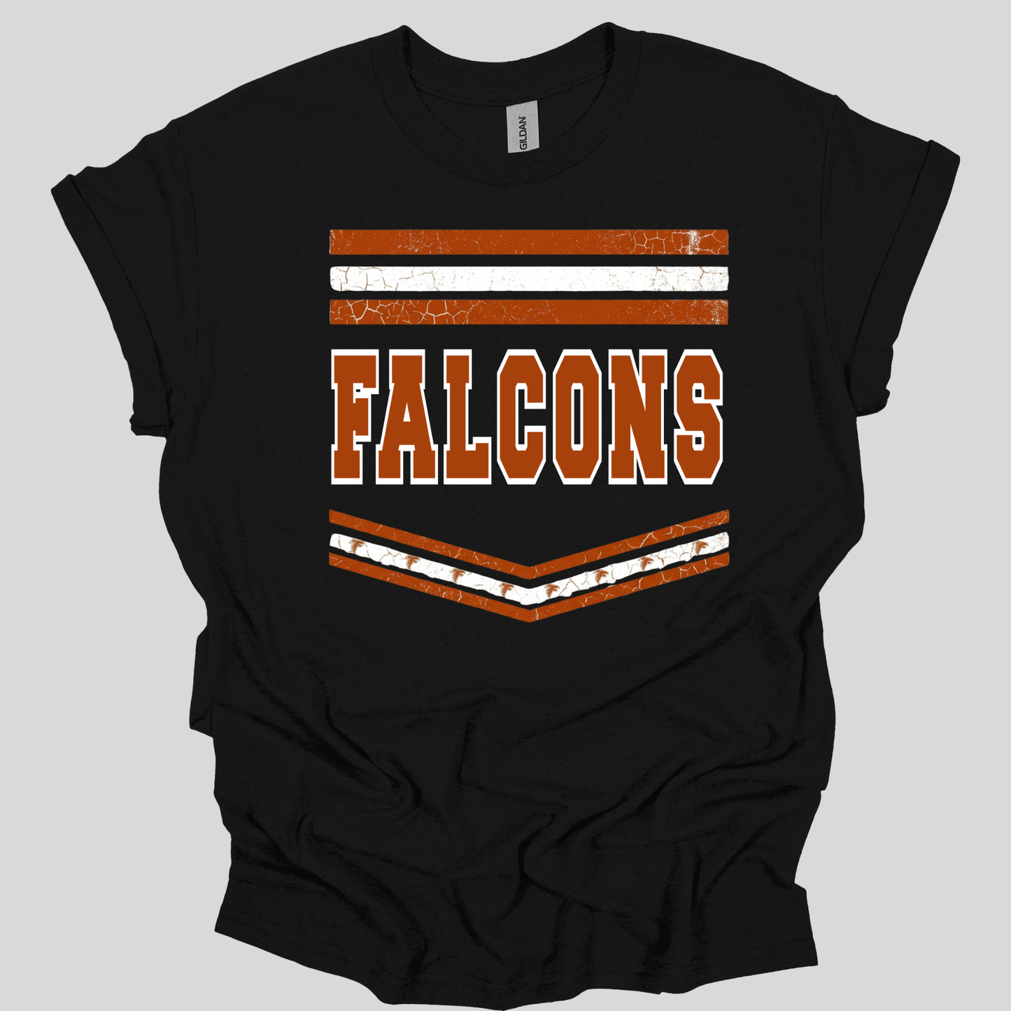 A black short-sleeve t-shirt with a distressed orange and white graphic on the front featuring the word 'FALCONS' and chevron stripes, shown on a solid gray background.
