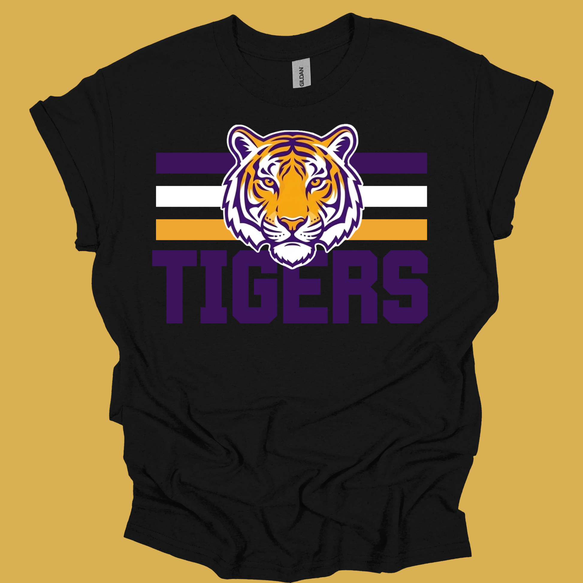 A black short-sleeve t-shirt with a purple, white, and orange tiger graphic and the word 'TIGERS' printed on the front, displayed against a solid mustard yellow background.