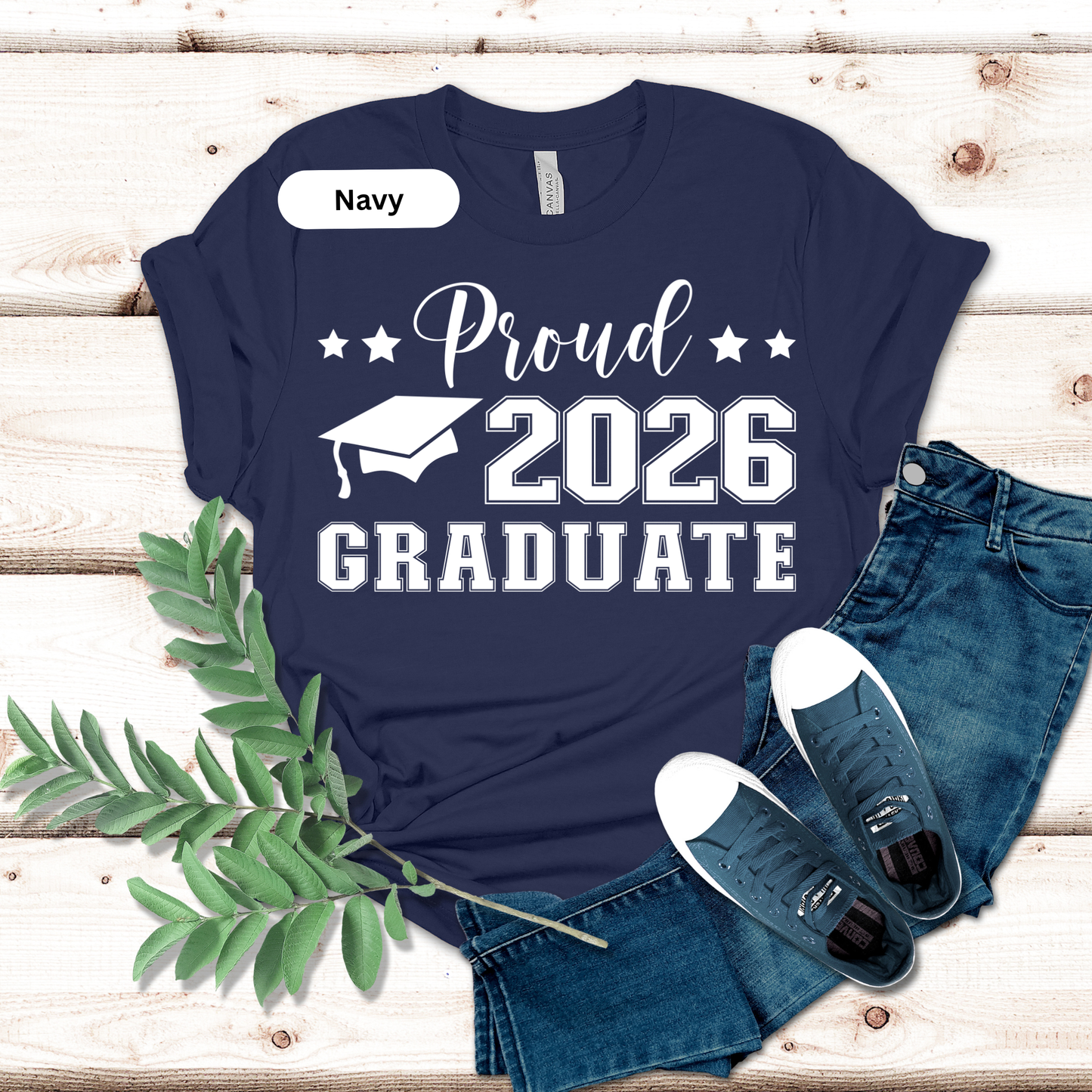 Navy t-shirt with 'Proud 2026 Graduate' text on a wooden surface with jeans and shoes.