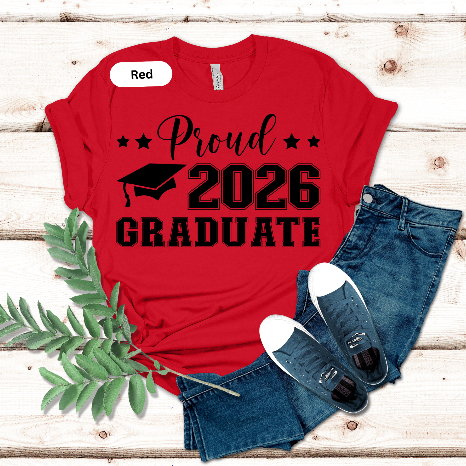 Red t-shirt with 'Proud 2026 Graduate' text, blue jeans, and white sneakers on a wooden surface.