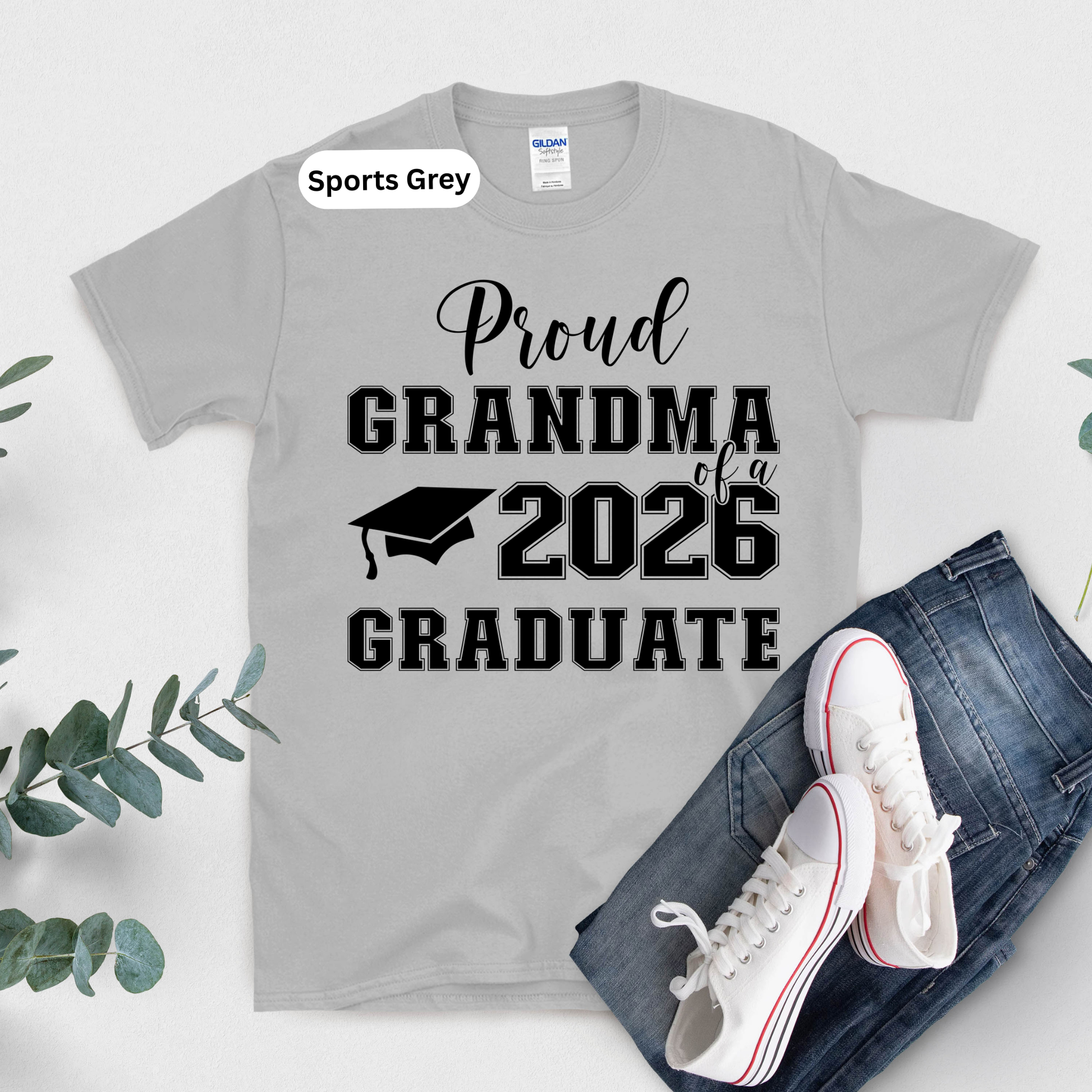Gray t-shirt with 'Proud Grandma of a 2026 Graduate' text and graduation cap graphic, displayed with jeans and sneakers.