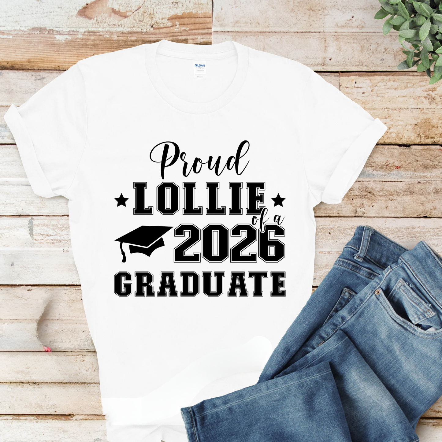 White t-shirt with 'Proud Lollie of a 2026 Graduate' text on a wooden surface with jeans.