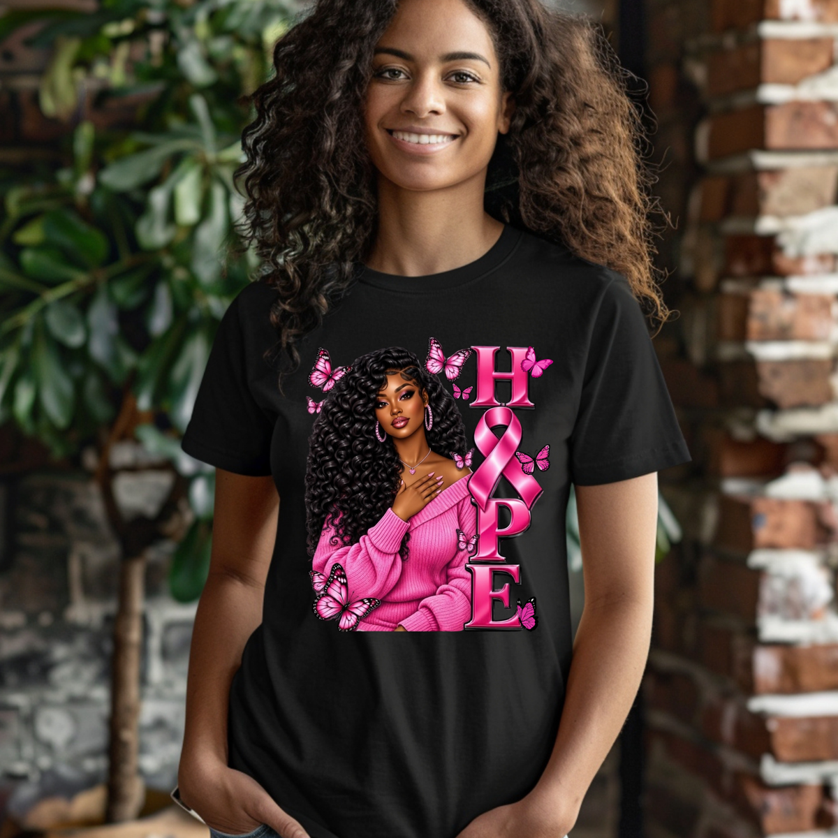 A woman wearing a black short-sleeve t-shirt with a pink graphic that reads 'Breast Cancer WARRIOR' with a pink ribbon and boxing gloves, paired with blue jeans against a white background.
