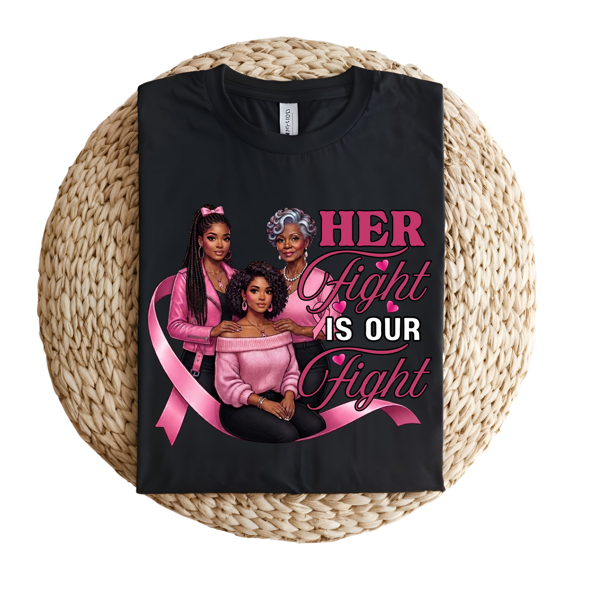 A black short-sleeve T-shirt laid flat on a round woven straw mat, featuring a large pink and white graphic that reads “I AM A SURVIVOR” with pink awareness ribbons, butterflies, and hearts.