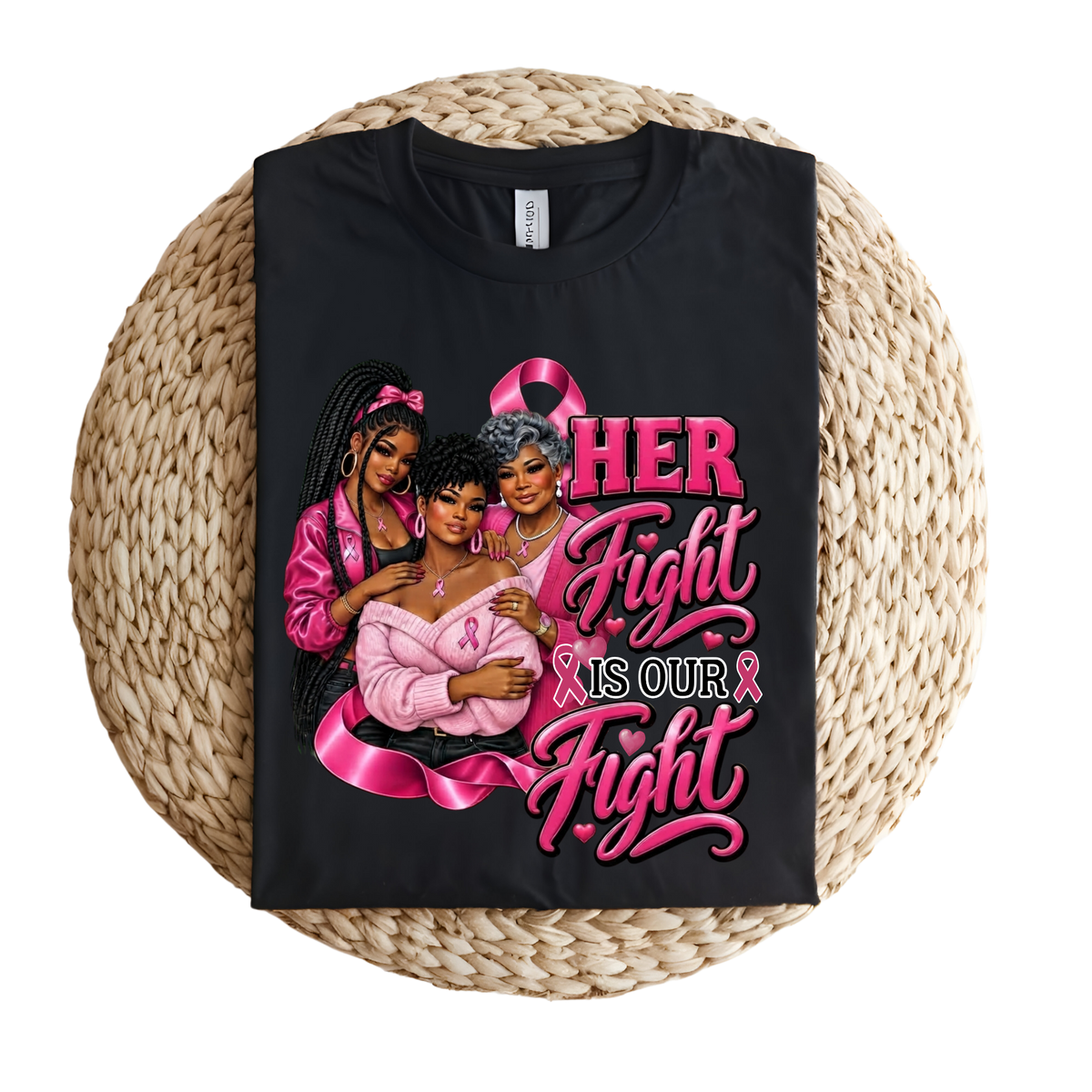 A black short-sleeve T-shirt laid flat on a round woven straw mat, featuring a large pink and multicolored graphic with three women and the text 'HER Fight IS OUR Fight' with pink awareness ribbons.