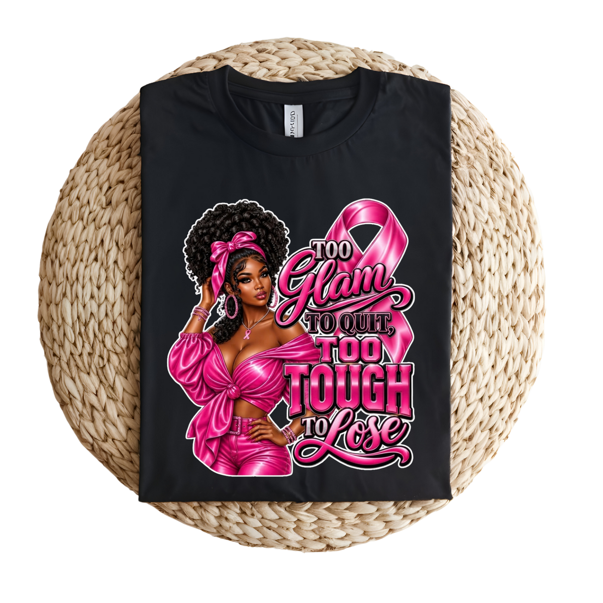 A black short-sleeve T-shirt laid flat on a round woven straw mat, featuring a pink graphic with a ribbon, boxing gloves, and the words 'Breast Cancer WARRIOR' in pink lettering.