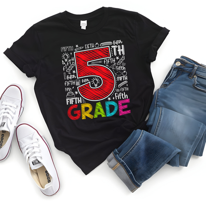 A black graphic t-shirt featuring a colorful '5th Grade' design, styled in a flat lay with blue jeans and white sneakers on a white background.