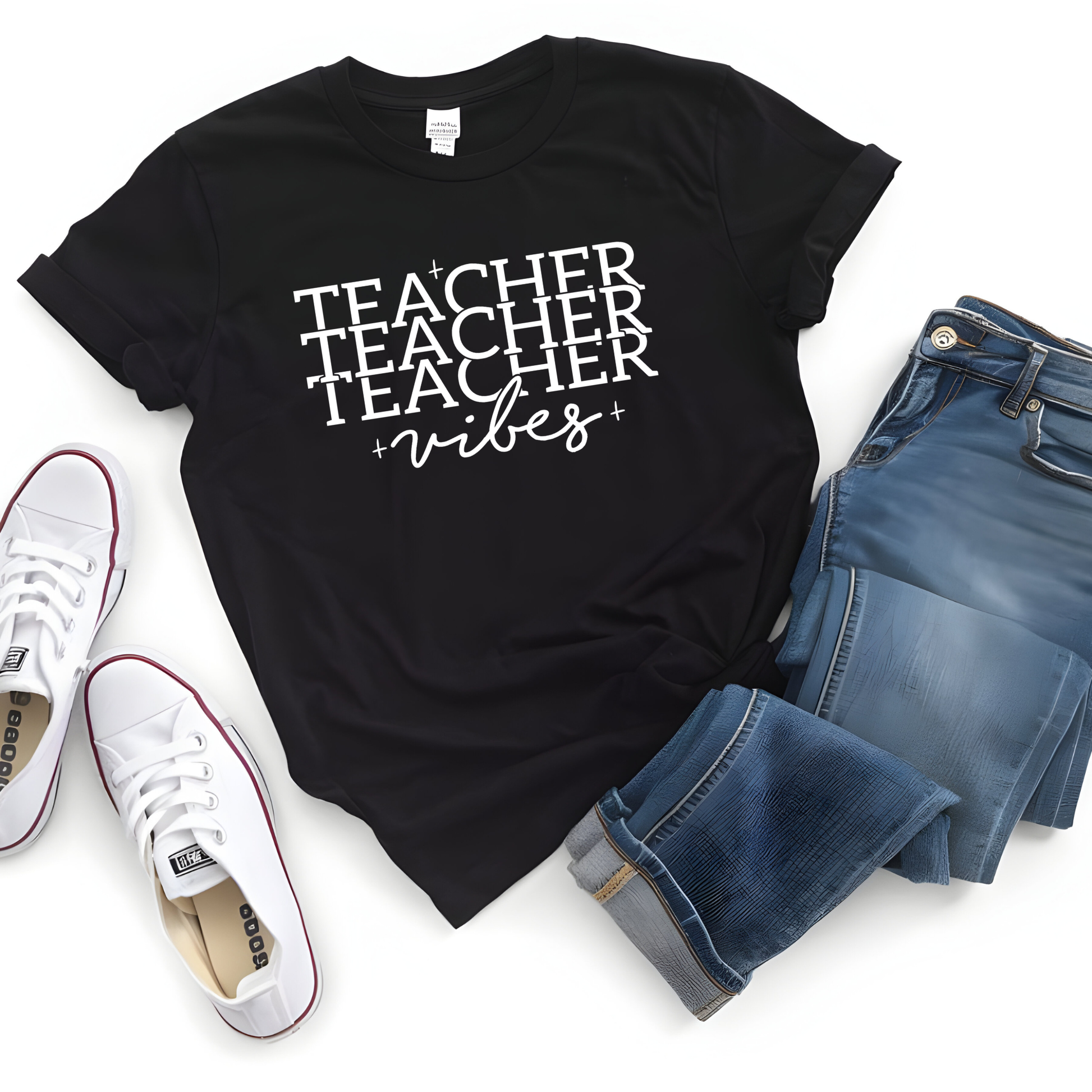 A black short-sleeve graphic T-shirt with the words 'TEACHER TEACHER vibes' printed in white, styled in a flat lay with blue jeans, white sneakers, and a white background.